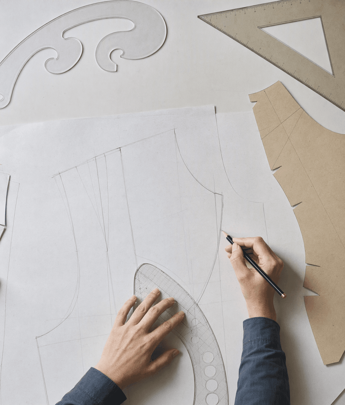 Hands drafting a bodice on the table with a french curve and a sloper